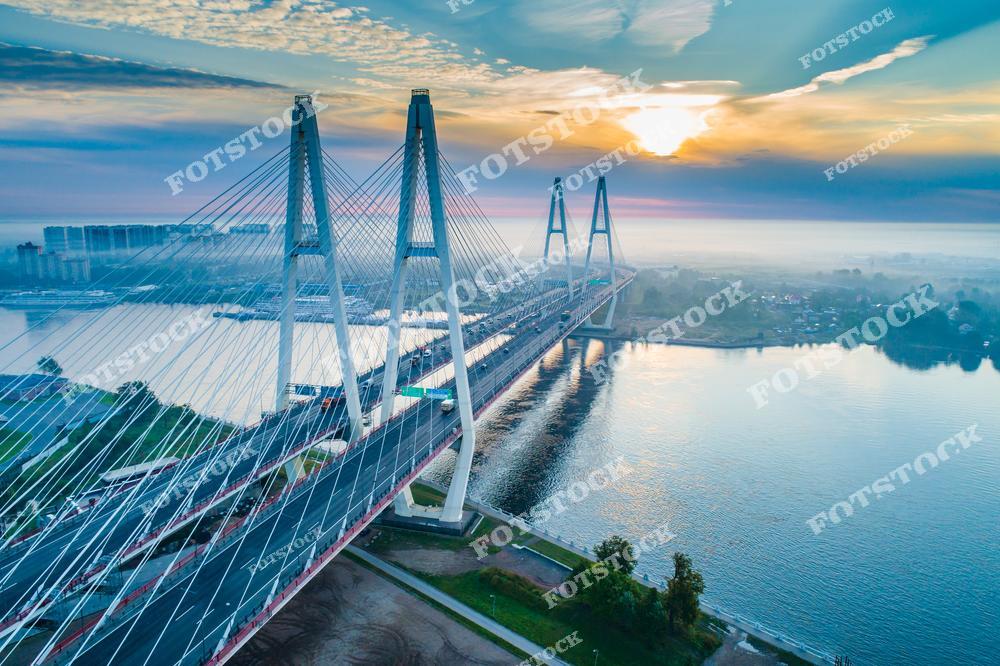 Фотография ночной панорамы Санкт-Петербург, Россия. На фото изображён вантовый Обуховский мост, освещённый огнями ночного города. Фотоснимок передаёт атмосферу современного Петербурга: подсветка моста, отражения света на воде и тёмное небо подчёркивают масштаб инженерного сооружения. Это изображение демонстрирует архитектуру транспортной инфраструктуры и ночной облик Санкт-Петербурга как крупного мегаполиса. Иллюстрация может использоваться как визуальный материал, посвящённый мостам и городским панорамам России.